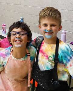 Two Boys with frosting on their face wearing aprons at CA Camps