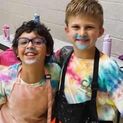 Two Boys with frosting on their face wearing aprons at CA Camps